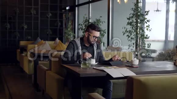英俊的宽容的男人坐在咖啡馆里喝着一杯绿茶视频的预览图