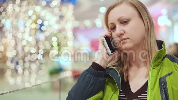 女人在智能手机上说话惊讶不已她正站在商场里一个灯泡不聚焦圣诞节的心情视频的预览图