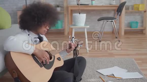 有非洲发型的非洲裔美国妇女的肖像弹吉他坐在地板上视频的预览图