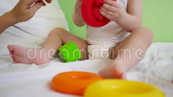 宝宝和妈妈在床上玩五颜六色的玩具孩子们在白色的床上玩里面有红色和绿色的立方体和戒指视频的预览图