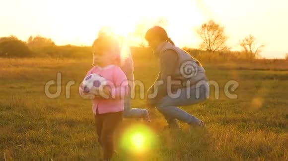 妈妈和小女儿在舞会上玩慢动作快乐的孩子在草地上用球跑步扔足球家庭视频的预览图
