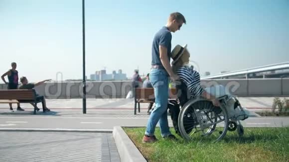 一个男人帮助一个坐轮椅的女孩从路边下到柏油路一个男人推着轮椅视频的预览图