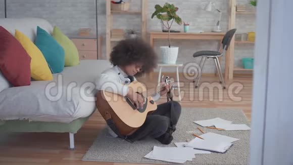非洲裔美国妇女有非洲发型弹吉他坐在地板上视频的预览图