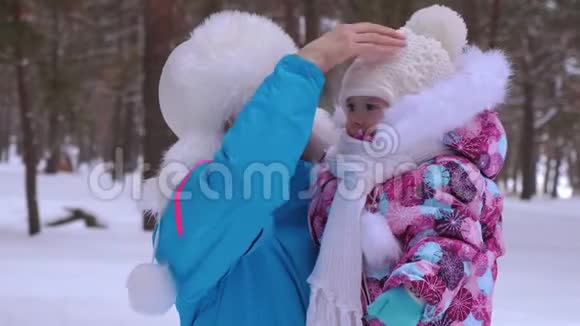 妈妈把她的小女儿抱在怀里在冬天把她的帽子拉直寒冷的天气健康散步视频的预览图