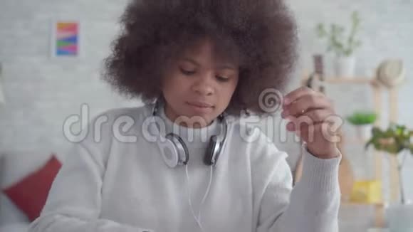 美国黑人妇女的肖像留着非洲发型带着耳机听音乐视频的预览图