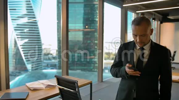 积极主动的企业家穿着正式西装站在窗边写短信视频的预览图