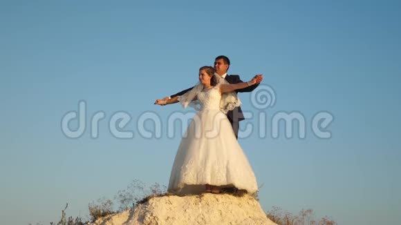 幸福的新娘和新郎拥抱和翱翔同时伸直双手在蓝天上微笑浪漫之旅视频的预览图