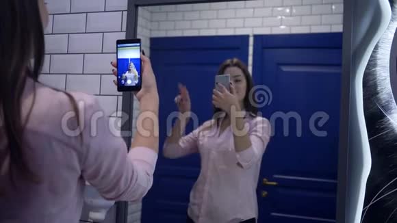 漂亮的女孩在镜子前摆姿势用手机在洗手间拍照视频的预览图