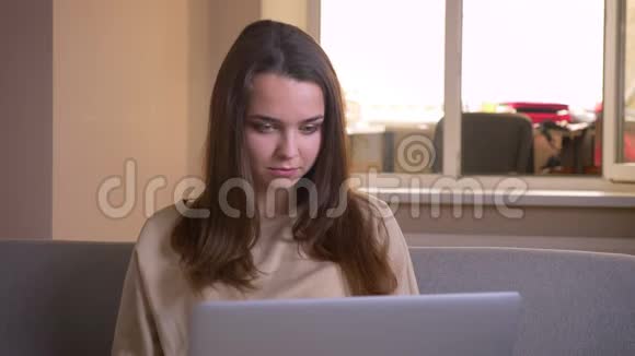 使用笔记本电脑和在室内沙发上看电影的年轻白种人女性的特写镜头视频的预览图