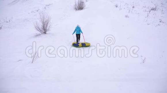 女孩爬上高高的雪山手里拿着雪碟女人在冬天玩雪橇山区度假胜地视频的预览图