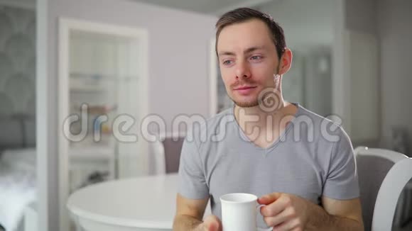 年轻风趣的男人在家里的厨房喝茶转过脸对着镜头微笑视频的预览图