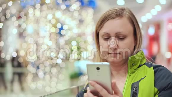 一位女士正在智能手机应用程序中写信息她站在商场里背景是一个灯泡视频的预览图