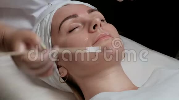 专业美容师在美容院将化妆面膜敷于女性颈部使用透明凝胶的程序视频的预览图