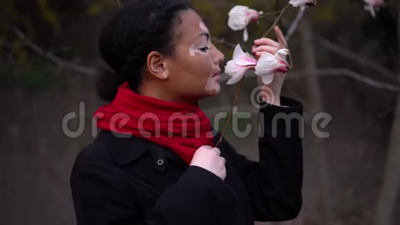 美丽的非洲女孩与白癜风站在街上闻春花木兰春天开花了视频的预览图