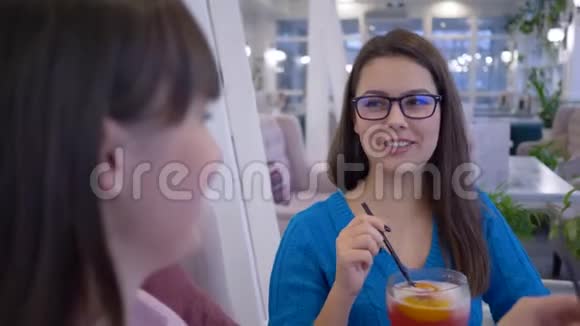 在周末的咖啡馆午餐时戴眼镜的妇女通过吸管交流和喝鸡尾酒视频的预览图