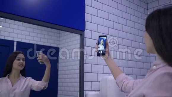 漂亮的女人被拍在智能手机上站在洗手间的镜子前视频的预览图