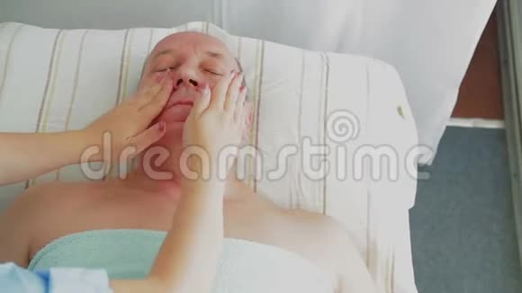 女美容师在一家水疗沙龙里给男人做一次坚定的面部按摩视频的预览图