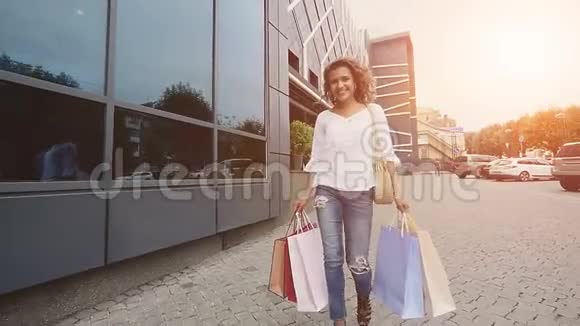 有魅力的年轻女人在城里带着购物袋慢动作阳光背景视频的预览图