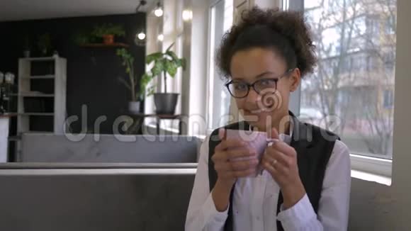 在闲暇时间在咖啡馆里为快乐的黑人少女戴上杯中杯热饮特写视频的预览图