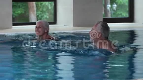 快乐的老年夫妇在酒店室内游泳池游泳视频的预览图