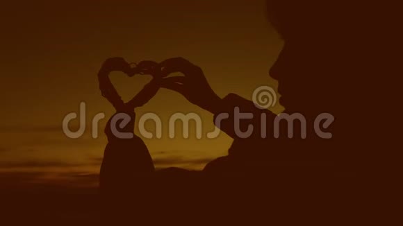 女孩在日落时双手捧着心浪漫又有爱心的女人视频的预览图