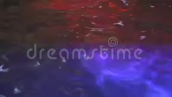 游泳池的水面在五颜六色的灯光下晚上的水上聚会涟漪中闪烁着五彩的光芒视频的预览图