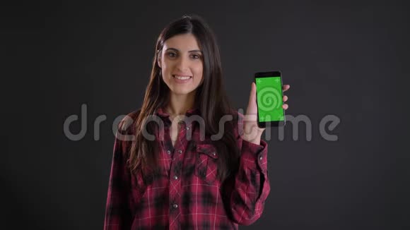 年轻的白种人长发女孩的肖像微笑着显示绿色屏幕的智能手机黑色背景视频的预览图