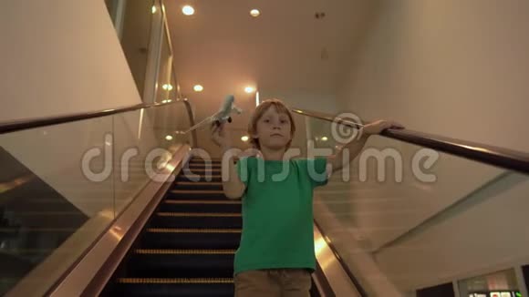 小男孩手里拿着白色的玩具飞机走下自动扶梯自由概念童年观念儿童视频的预览图