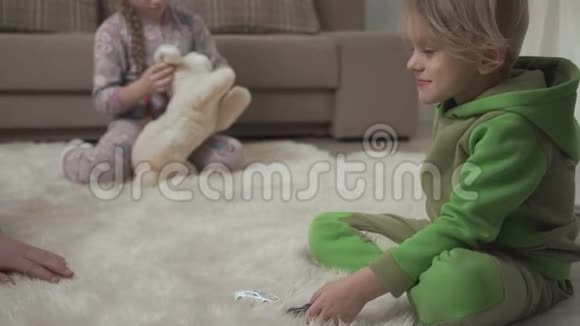 两个可爱的孩子躺在地上毛茸茸的地毯上在家玩玩具男性手触摸鼻子视频的预览图