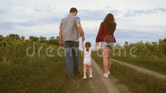小女儿跳着手牵着爸爸妈妈一家人带着小孩走在路上在田野旁欢笑视频的预览图