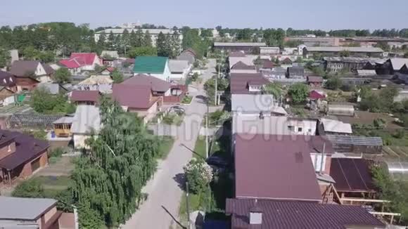 在夏日的蓝天上鸟瞰村庄的房屋和乡村道路周围环绕着绿树股票视频的预览图