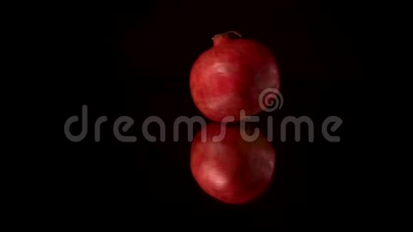 鲜红色的石榴在黑色的镜桌上旋转翻滚黑色背景视频的预览图