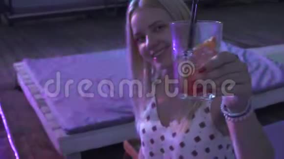 孤独的女孩在一家夜总会喝鸡尾酒坐在夏季露台上年轻的金发女郎喜欢俱乐部的气氛视频的预览图