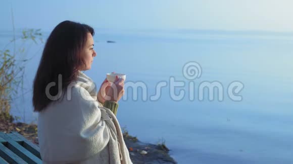 美丽的女人喝着裹着格子布的茶看着河岸上的日出视频的预览图