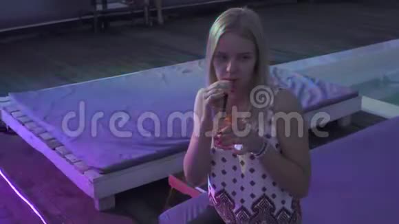 美丽的女孩坐在夏季露台的酒吧里喝鸡尾酒可爱孤独的金发女郎在视频的预览图