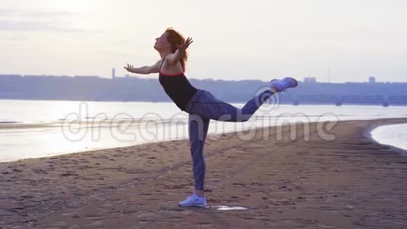 黄色动作一个红头发的中年妇女在一条大河的沙岸上做体操视频的预览图