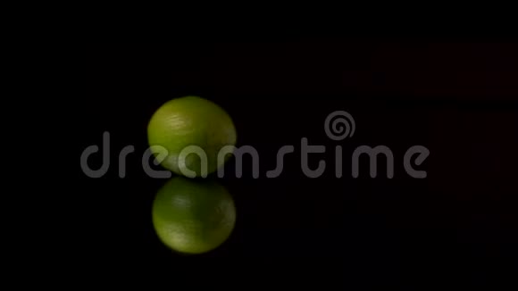 绿色新鲜石灰或绿色柠檬在镜子上的黑色背景上旋转视频的预览图