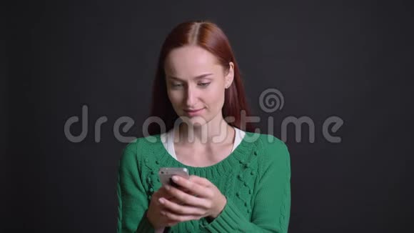 为一位长相迷人的白种人女性的特写画像她的红头发在手机上打字看着镜头开心地笑着视频的预览图