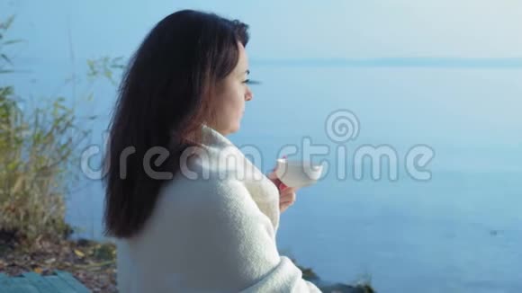 特写镜头美丽的女人坐在草地上在河岸边喝杯茶看日出视频的预览图