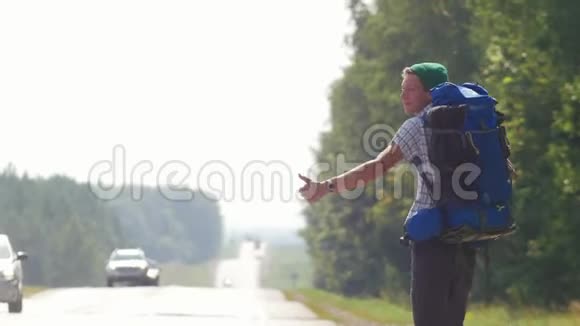 一个年轻的男性搭便车者带着一个大背包变焦从摄像机一路走来视频的预览图