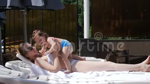 母亲和女儿在游泳池旁的阳光下放松视频的预览图