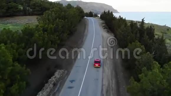 在靠近海洋或海洋的道路上乘坐小红色复古车视频的预览图