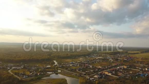 蓝蒙蒙的天空背景下绿色森林穿越河流的大村舍的鸟瞰图视频的预览图