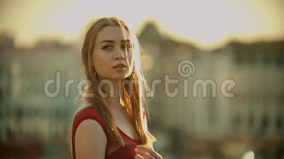 一位年轻有灵感的女士穿着红色连衣裙站在屋顶上在日落时为相机摆姿势视频的预览图