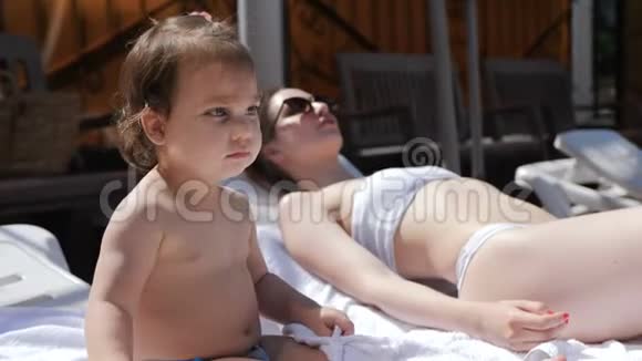 母亲和女儿在游泳池旁的阳光下放松视频的预览图