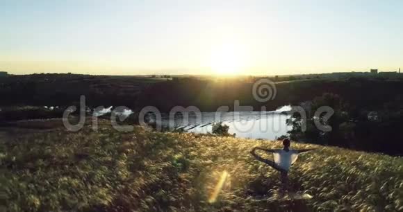 日落时在美丽的草地上做瑜伽的女孩慢动作视频的预览图