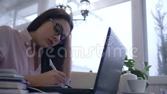 由于学习过度疲惫的女学生眼镜使用笔记本电脑从网上教学准备考试视频的预览图