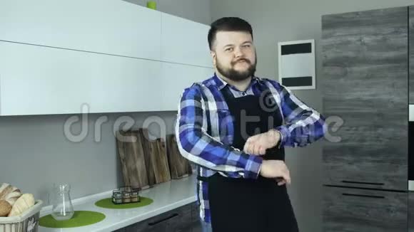 一个穿着围裙的大胡子厨师在现代化的厨房里看着镜头视频的预览图