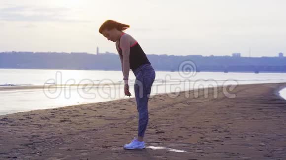 慢动作一个红头发的中年妇女在一条大河的沙岸上做体操视频的预览图
