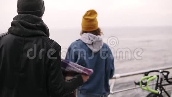 一对年轻夫妇站在海上木墩上拥抱时把格子布搭在女朋友的肩上视频的预览图
